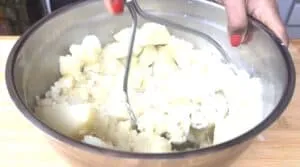 Hand mashing boiled potatoes in a metal bowl for creamy homemade mashed potatoes.